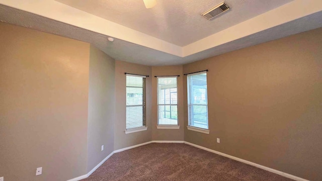 unfurnished room featuring dark colored carpet, a raised ceiling, visible vents, and baseboards