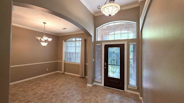 foyer with tile patterned flooring, a notable chandelier, crown molding, baseboards, and arched walkways