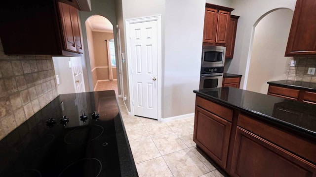 kitchen featuring decorative backsplash, light tile patterned floors, dark countertops, arched walkways, and appliances with stainless steel finishes