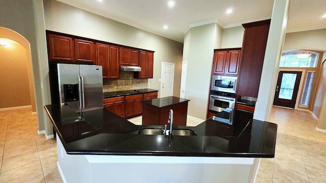 kitchen with a sink, stainless steel appliances, under cabinet range hood, a spacious island, and backsplash