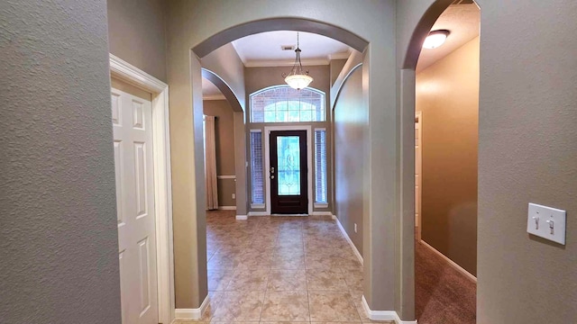 foyer featuring baseboards, ornamental molding, arched walkways, and a textured wall