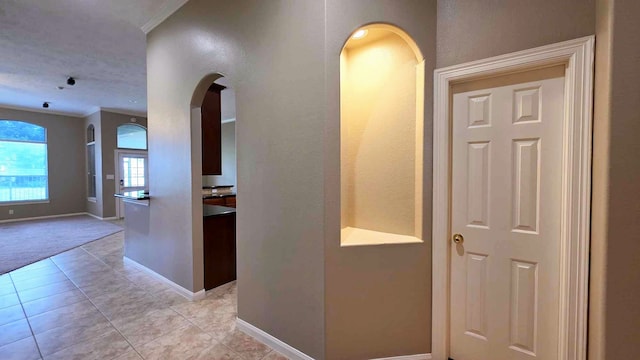 corridor with baseboards, arched walkways, light tile patterned flooring, ornamental molding, and light carpet