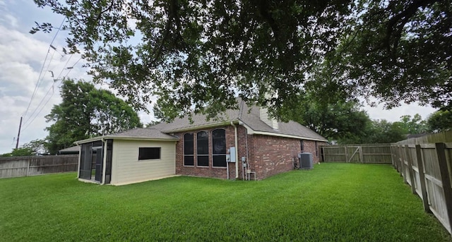 rear view of house featuring a fenced backyard, a yard, brick siding, and a sunroom