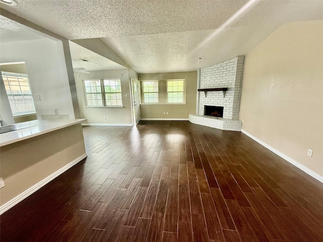 8818 Fern Valley Dr, Houston, TX 77044 - unfurnished living room with a textured ceiling, dark wood finished floors, a brick fireplace, baseboards, and vaulted ceiling