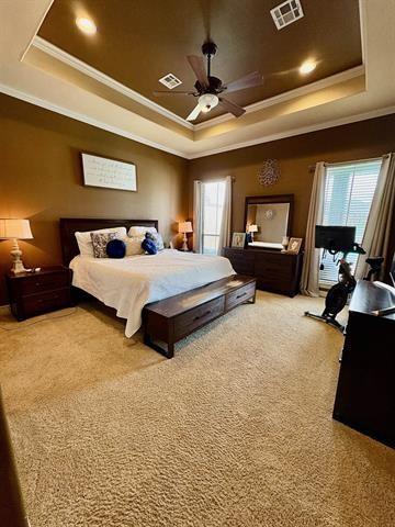 bedroom with a raised ceiling, visible vents, and ornamental molding