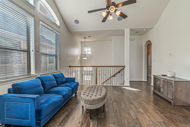 living area featuring lofted ceiling, ceiling fan, arched walkways, baseboards, and dark wood-style flooring