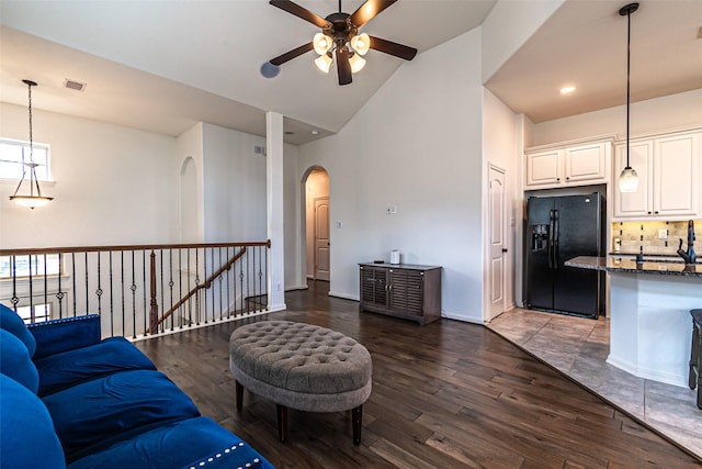 living area featuring wood finished floors, visible vents, a ceiling fan, arched walkways, and high vaulted ceiling