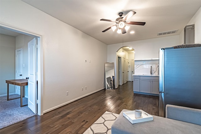 interior space featuring a ceiling fan, arched walkways, baseboards, dark wood-type flooring, and visible vents