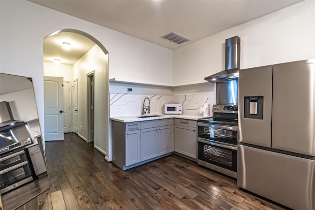 kitchen featuring stainless steel appliances, wall chimney range hood, visible vents, arched walkways, and gray cabinetry
