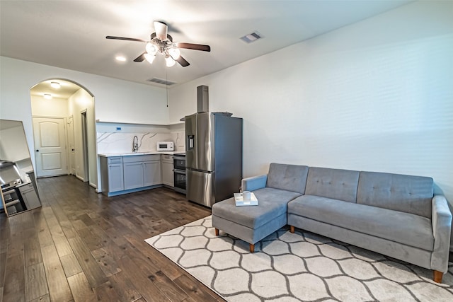 living area featuring dark wood-type flooring, arched walkways, visible vents, and ceiling fan