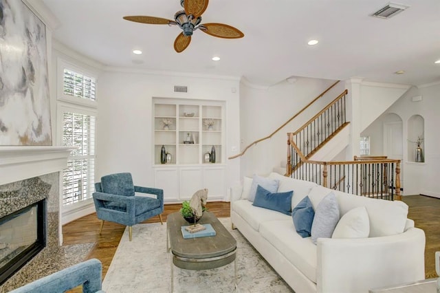 living room with a high end fireplace, wood finished floors, visible vents, and ceiling fan