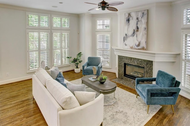 living room featuring a premium fireplace, wood finished floors, baseboards, and ceiling fan