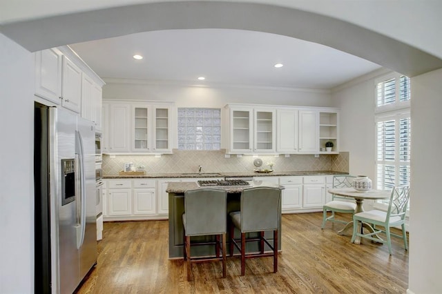 kitchen with stainless steel refrigerator with ice dispenser, a kitchen island, ornamental molding, and tasteful backsplash