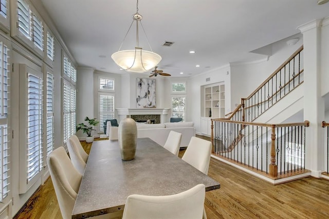 dining space with wood finished floors, visible vents, ornamental molding, a fireplace, and ceiling fan