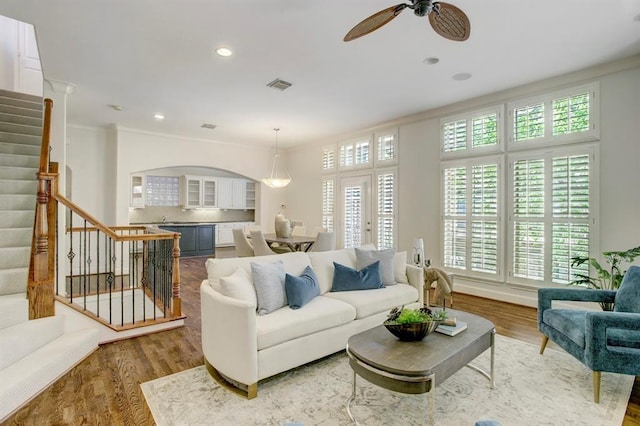 living room featuring crown molding, a ceiling fan, wood finished floors, stairs, and visible vents