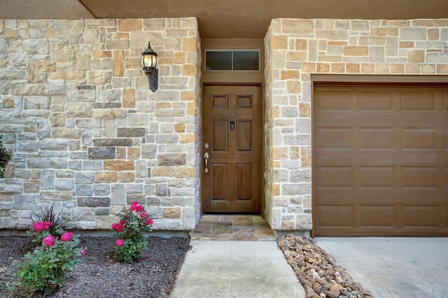 view of exterior entry featuring an attached garage and stone siding
