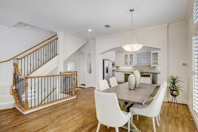dining room featuring arched walkways, light wood finished floors, ornamental molding, visible vents, and recessed lighting
