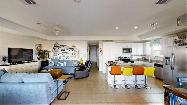 living area with light tile patterned flooring, visible vents, and a raised ceiling