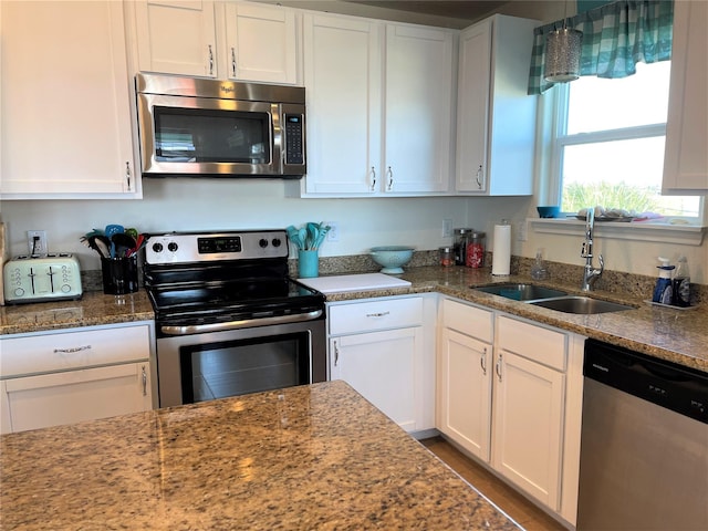 kitchen with white cabinets, stainless steel appliances, a sink, decorative light fixtures, and stone counters