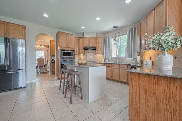 kitchen with a sink, light tile patterned flooring, tasteful backsplash, arched walkways, and appliances with stainless steel finishes