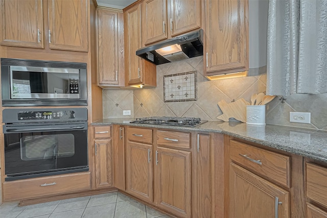 kitchen with light tile patterned floors, tasteful backsplash, appliances with stainless steel finishes, under cabinet range hood, and stone counters