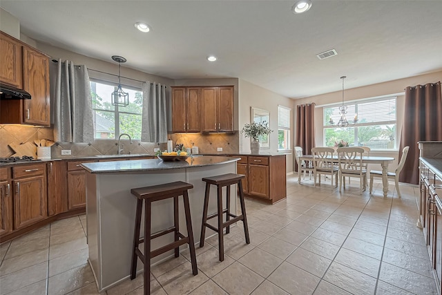 kitchen with an inviting chandelier, a sink, a kitchen island, and brown cabinetry