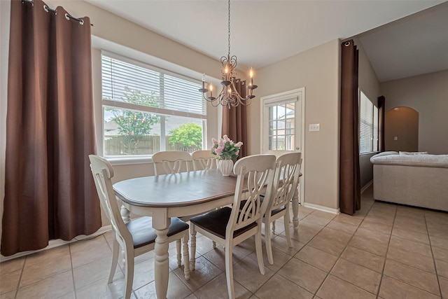dining room featuring light tile patterned floors, arched walkways, a notable chandelier, and baseboards