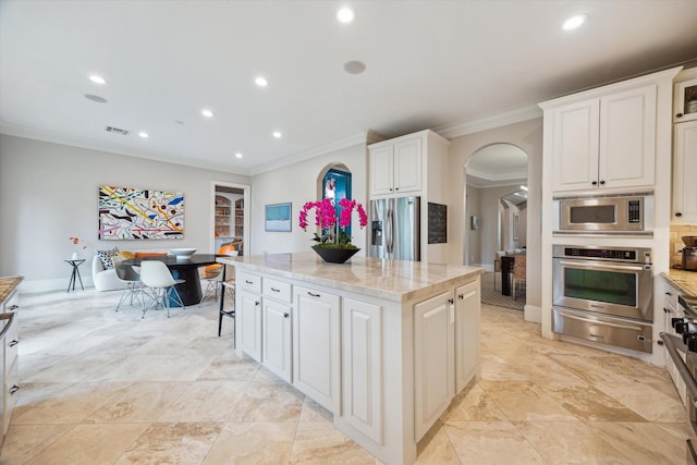kitchen with arched walkways, a center island, stainless steel appliances, ornamental molding, and a warming drawer