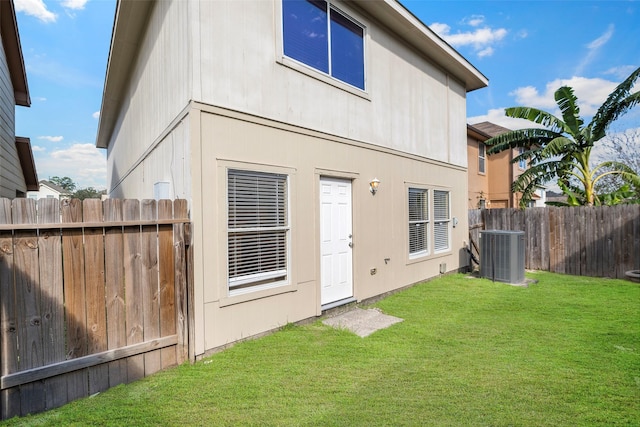 back of property with fence, a lawn, and central AC