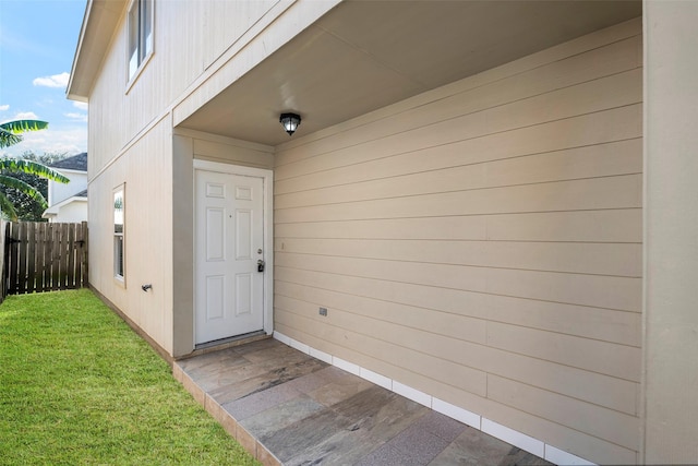view of exterior entry featuring a lawn and fence