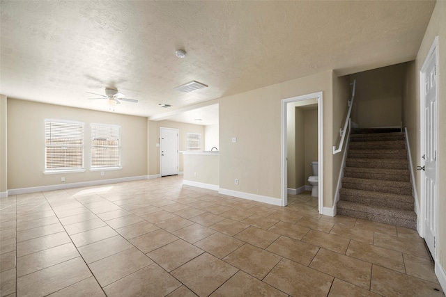 unfurnished living room with stairway, a ceiling fan, a textured ceiling, a healthy amount of sunlight, and visible vents