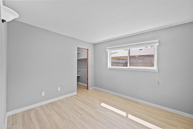 unfurnished bedroom with a spacious closet, baseboards, wood finished floors, and a closet
