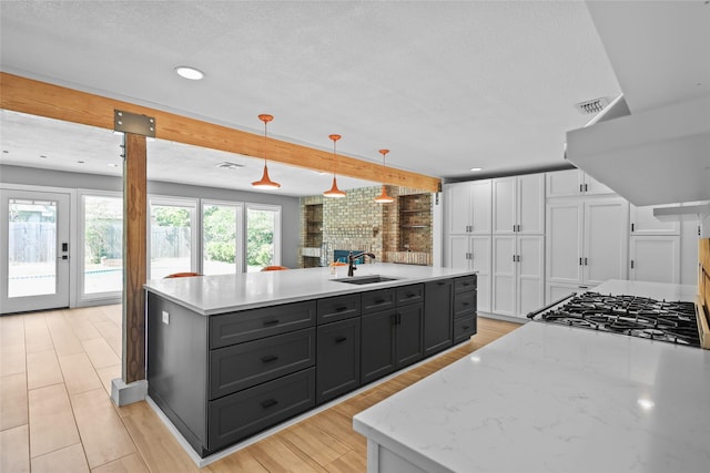 kitchen featuring a sink, hanging light fixtures, an island with sink, white cabinetry, and visible vents
