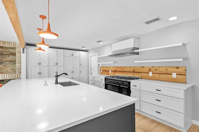 kitchen featuring white cabinets, wall chimney exhaust hood, a sink, and double oven range