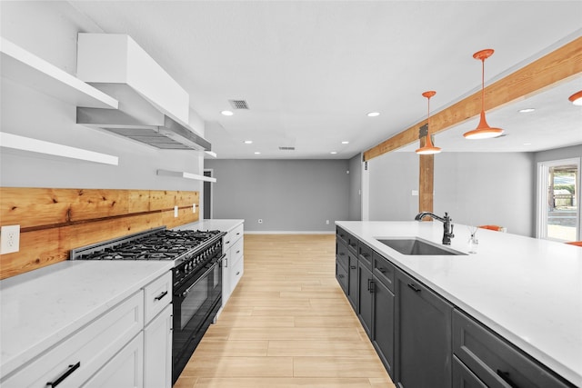 kitchen featuring high end stove, visible vents, a sink, wall chimney exhaust hood, and light wood-style flooring