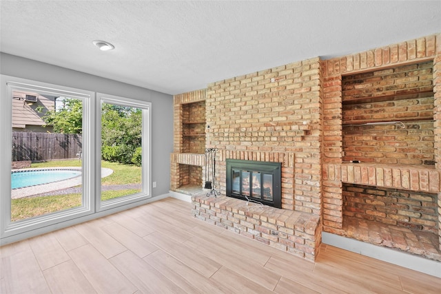 unfurnished living room with a fireplace, wood finished floors, a textured ceiling, and baseboards