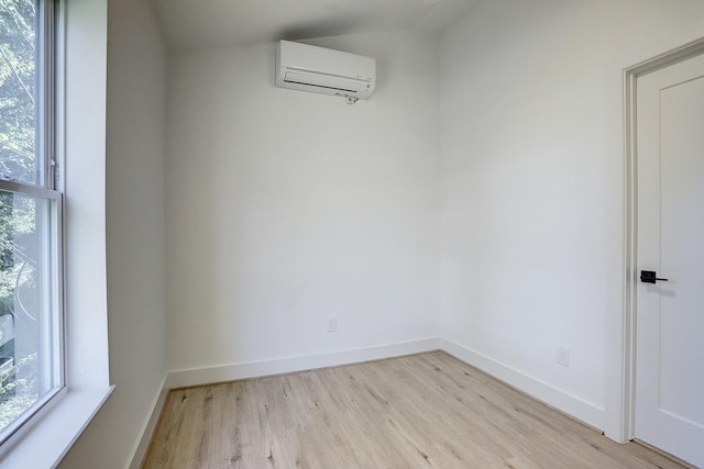 empty room featuring a wall mounted AC, plenty of natural light, light wood finished floors, and baseboards