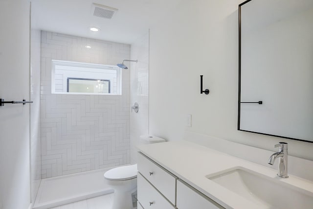 full bath featuring toilet, vanity, visible vents, and tiled shower