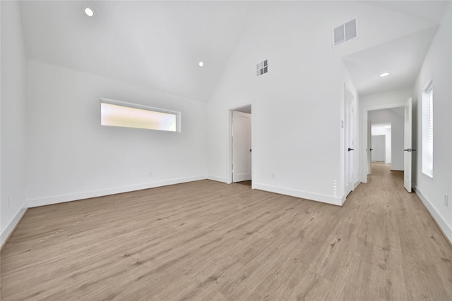 unfurnished bedroom with baseboards, visible vents, light wood finished floors, and high vaulted ceiling