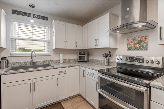 kitchen featuring wall chimney range hood, a sink, light wood finished floors, white cabinets, and range with two ovens
