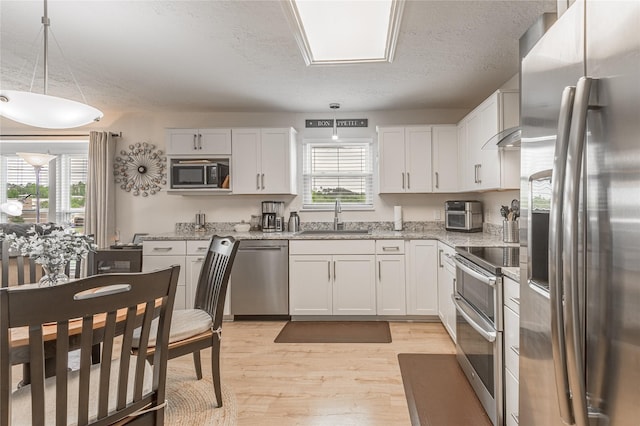kitchen with a sink, light wood-style floors, a wealth of natural light, stainless steel appliances, and white cabinets