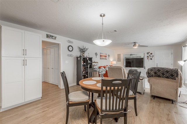 dining area featuring visible vents, light wood-type flooring, baseboards, a textured ceiling, and ceiling fan