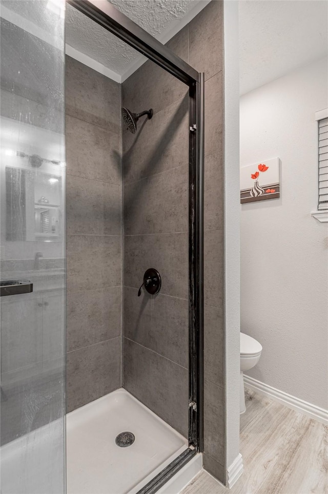 bathroom with baseboards, wood finished floors, a shower stall, and toilet