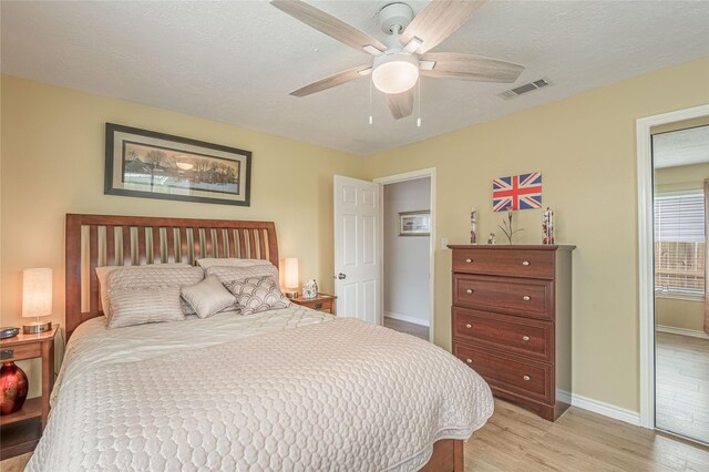bedroom featuring a textured ceiling, visible vents, baseboards, light wood finished floors, and a ceiling fan