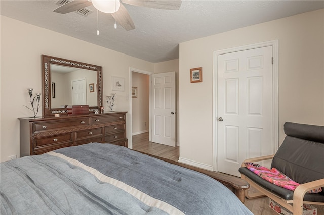 bedroom with a ceiling fan, wood finished floors, a textured ceiling, baseboards, and visible vents