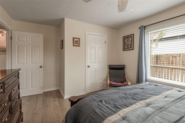 bedroom featuring light wood-style flooring, a textured ceiling, a ceiling fan, and baseboards