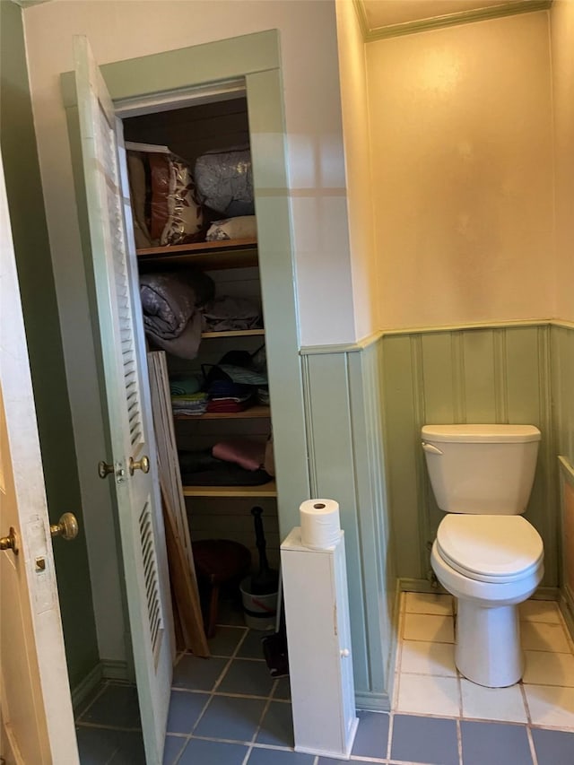 bathroom featuring tile patterned flooring, toilet, a wainscoted wall, and a decorative wall