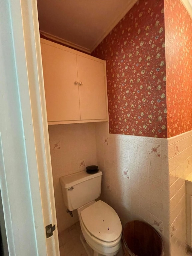 bathroom featuring tile walls, wallpapered walls, a wainscoted wall, and toilet