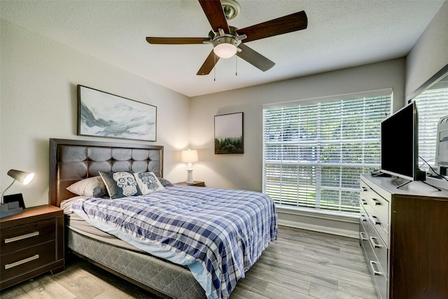 bedroom with a textured ceiling, a ceiling fan, and light wood finished floors