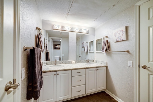 full bath featuring toilet, double vanity, a sink, and a textured wall
